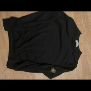 Svart Stone Island tröja med patch - Svart långärmad tröja från Stone Island med klassisk rund hals och ikonisk avtagbar patch på vänster ärm. Tröjan är i mjuk bomull och har en clean, stilren look som passar perfekt till streetwear-stilen.