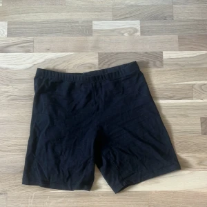 Svarta cykelshorts från 157 - Svarta cykelshorts från 157 i mjuk och stretchig bomullsmix. De har en enkel och clean design med elastisk midja och sitter tight mot kroppen. Perfekta för en sportig look eller till vardagsoutfiten.