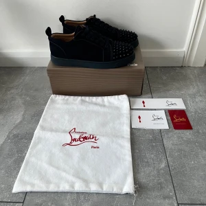 Marinblåa Christian Louboutin - Säljer ett par marinblåa sneakers från Christian Louboutin med coola svarta nitar på tån. En nit har gått bort från ena skon men inget som syns så mycket alls. Skorna är i mocka och kommer med originalpåse och äkthetskort. 