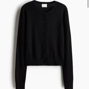 Svart kofta från H&M med knappar - En klassisk svart kofta från H&M i storlek XS. Koftan har rund halsringning, långa ärmar och knäppning framtill med svarta knappar. Tillverkad i mjuk bomullsmix som är skön att bära. Perfekt att slänga över en t-shirt eller linne.