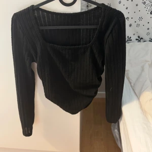 Svart ribbad topp från SHEIN - Svart långärmad topp från SHEIN med ribbad struktur och fyrkantig ringning. Toppen är figurnära och har en enkel, stilren design som passar till många olika outfits. Tillverkad i mjukt och stretchigt material för en bekväm känsla.