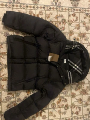 Svart bb pufferjacka - Svart bb pufferjacak i storlek m fast passar även L med tagg på och randiga detaljer på luvan och top kavlite