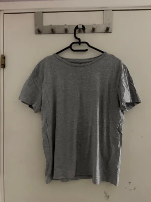 Grå basic t-shirt i bomull - Enkel grå t-shirt med rund hals och korta ärmar. Tillverkad i mjuk bomull som känns skön mot huden. Perfekt till jeans eller shorts för en clean och avslappnad look.