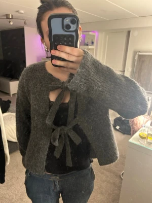 Grå stickad kofta med knyt - Mysig grå stickad kofta med två stora knytband framtill. Koftan har lång ärm och en lite lösare passform, perfekt att slänga över ett linne eller t-shirt. Den är från GinaTricot. Använt fåtal gånger. Pris kan diskuteras.