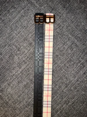  Burberry bälten med B-spänne - Säljer 1 Burberry bälten med ikoniskt B-spänne i guld. Ena bältet är svart med präglat rutmönster och riddare, det andra är beige med klassiskt rutig design i rött, grått och vitt. Båda är i skinn och har exklusiv känsla. Perfekt accessoar för att lyfta din outfit. Finns 2 st 
