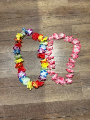 Färgglada hawaiikransar i syntet - Två hawaiikransar i syntetmaterial, en i regnbågens alla färger och en i rosa och vitt. Perfekta till temafest eller sommarhäng. Blommorna är stora och sitter tätt för en maxad look.