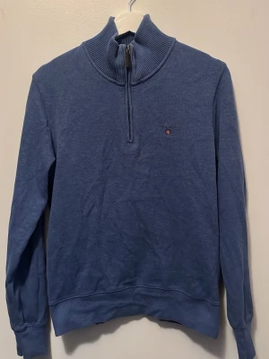 Blå half zip tröja från Gant - Snygg blå långärmad tröja från Gant med ribbad hög krage och half zip-dragkedja. Liten broderad logga på bröstet. Perfekt till chill dagar och enkel att matcha med jeans eller chinos.