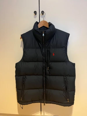 Navyblå dunväst från Ralph Lauren - Säljer en navyblå dunväst från Ralph Lauren. Har knappt använts sen den köptes så skicket är som nytt. Storlek är Medium. Jag är 183cm och den passar mig bra.