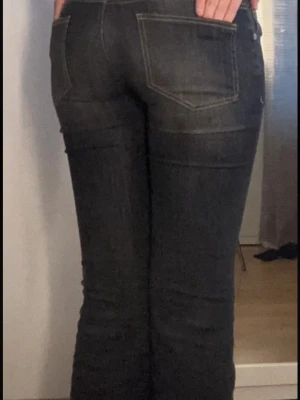 Y2K low waist jeans  - Säljer ett par snygga Replay bootcut jeans i mörkgrå tvätt med ljusa slitningar framtill. Jeansen har låg midja, klassiska fem fickor och kontrastsömmar. Materialet är jeans med stretch för skön passform. Perfekt för dig som gillar retrovibbar och vill ha ett par jeans med lite extra attityd.