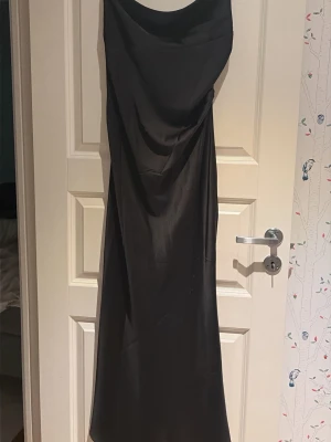 Svart långklänning Gina Tricot 36 - Säljer en svart långklänning från Gina Tricot i storlek 36. Klänningen har en snygg draperad halsringning och spetsdetaljer på insidan. Materialet är glansigt och känns lyxigt, perfekt för dig som vill ha en elegant look. Aldrig använd