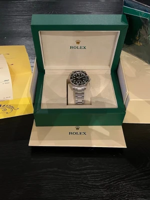 Rolex Submariner stål svart urtavla - Säljer en ikonisk Rolex Submariner med svart urtavla och vridbar bezel. Klockan har ett robust armband i rostfritt stål och klassisk oyster-länk. Tydliga index och datumfönster vid klockan tre. Perfekt för dig som gillar stilrena accessoarer.