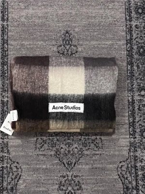 Rutig ull halsduk från Acne Studios - Säljer en sjukt snygg rutig halsduk från Acne Studios i mjuk ullmix. Västen har breda blockrutor i brunt, beige, grått och svart, samt fransar nedtill för extra stilpoäng. Perfekt att slänga över en hoodie eller tröja för en chill look.