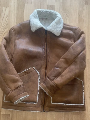 Brun teddyjacka med dragkedja - Säljer en brun teddyjacka med mjukt, vitt foder och krage i teddy. Jackan har stora fickor framtill och stängs med dragkedja. Perfekt för kalla dagar och ger en riktigt chill look.