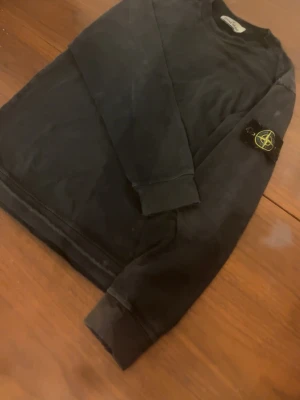 Svart sweatshirt från Stone Island - 100% äkta ba scanna koden den köpte för 3000kr Säljer en svart långärmad sweatshirt från Stone Island med den klassiska loggan på ärmen. Tröjan har rund halsringning och ribbade muddar vid ärmslut och nederkant. Perfekt för dig som gillar streetwear och vill ha något stilrent. OBS tröjan är lite urtvättad vilket jag personligen tycker ger den lite mer karaktär, men sen e den dock lite slitet i armen men inget som verkligen märks av vid användning 