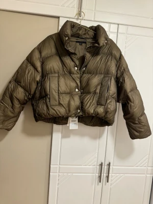 Olivgrön croppad pufferjacka från Zara - Säljer en olivgrön croppad pufferjacka från Zara. Jackan har hög krage, stora fickor framtill och stängs med både dragkedja och knappar. Oversized passform och riktigt fluffig look, perfekt för kalla dagar. Nypris 1190 kr 