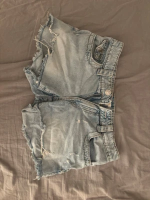 Ljusblå jeansshorts från Gina Tricot🫶🏻 - Säljer ett par ljusblå jeansshorts från Gina Tricot med råa, fransiga kanter och snygga slitningar. Shortsen har broderade bakfickor med paisleymönster och klassisk femficksdesign. Perfekta för sommaren och riktigt sköna att bära. Jätte snygga!🤍