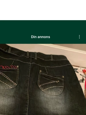 Fel i annons när den autoskrev.Blå jeanskjol med broderade detaljer detaljer - Unik svart jeanskjol med kontrastsömmar och broderade blommor och hexagoner i rött, vitt och svart på framsidan. Snygga fickor bak med dekorativa sömmar och röda detaljer. Perfekta för dig som vill sticka ut lite extra.