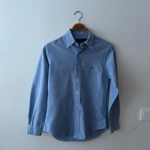 Ljusblå slim fit skjorta från Ralph Lauren - blå skjorta från Ralph Lauren i slim fit stretch oxford. Skjortan är i Medium och är perfekt till både sommaren och vintern, passar till mycket med sin lyxiga och normala look.