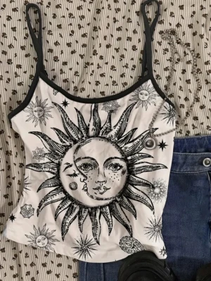 Vit och svart linnetopp med soltryck - Säljer en vit linnetopp med svarta tunna axelband och ett stort sol- och stjärnmönster i svart. Toppen har croppad passform och är perfekt för varma dagar. Materialet känns mjukt och lätt, och trycket ger en cool, bohemisk vibe.
