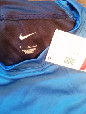 Blå Nike t-shirt  - Snygg blå t-shirt från Nike med klassisk vit swoosh-logga på bröstet. Tillverkad i lätt och ventilerande polyester, perfekt för träning eller sport. Enkel design med rund hals och korta ärmar, riktigt clean och sportig vibe. Stor i storlek, motsvarande XL