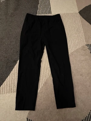 Svarta byxor med snörning Från HM - Svarta byxor med rak passform och elastisk midja med snörning. Byxorna har en enkel och clean look, perfekta för en chill stil. Materialet känns mjukt och bekvämt, passar till många olika outfits.