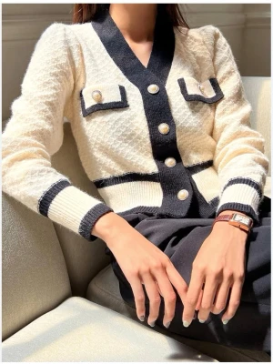 Vit och svart kofta från Holly & Whyte - Säljer en snygg vit kofta med svarta detaljer från Holly & Whyte. Koftan har dekorativa pärlknappar och ribbade muddar. Materialet är stickat och modellen är croppad med lång ärm och markerad midja. Använd fåtal gånger 