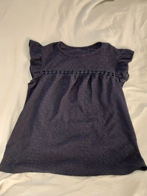 Mörkblå blus med volang från SHEIN - Säljer en mörkblå blus/topp  från SHEIN i storlek XS. Blusen har korta volangärmar och hålmönster. Bra skick! Katt finns I hemmet.