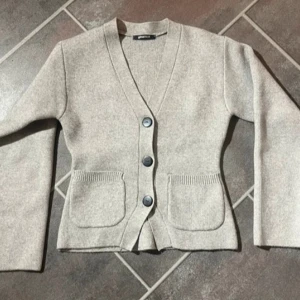  kofta med fickor och knappar - Säljer en kofta från Gina Tricot med v-ringning, stora svarta knappar och två praktiska fickor framtill. Koftan har lång ärm och är gjord i mjukt material som passar perfekt till lager på lager under höst och vår.