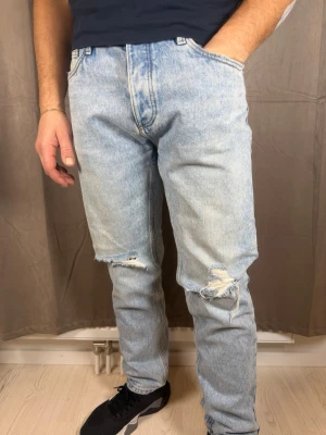 Ljusa ripped jeans från FSBN Denim - Säljer ett par ljusblå jeans från FSBN Denim med snygga slitningar och hål vid knäna. Modellen har rak passform och klassisk femficksdesign. Jeansen har en cool tvättad look och patch med schackmönster och gul logga bak. Perfekt för dig som gillar streetstyle.