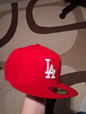 Röd LA Keps från New Era - Går fett med majoriteten av dina outfits! Köpt för 520kr (med frakt) Kommer inte till användning då det inte är min stil längre Storlek finns på tredje bilden. Den är använd men så gott som ny då jag tagit hand om den. 