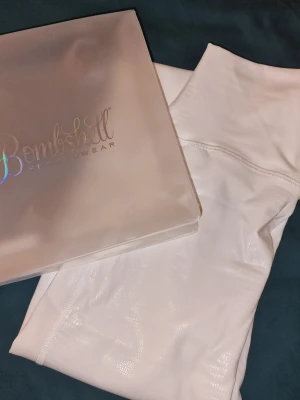 Vita leggings från Bombshell Sportswear - Vita leggings från Bombshell Sportswear white pyton. Sitter snyggt och bekvämt vilket är perfekt för träning & dans. Märkeslogga på linningen och originaltaggar kvar. Säljer även matchande sportbh.