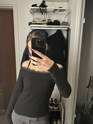 Svart offshoulder topp med spetskant - Säljer en svart offshoulder topp med lång ärm och snygg spetskant längs urringningen. Toppen är ribbad och har en tight passform som framhäver figuren. Perfekt för dig som gillar en enkel men ändå elegant stil.