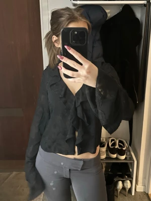 Volang blus med spets detalj - En svart snygg blus ifrån Nelly med volanger. Blusen har spets mönster över hela toppen. Och knappar som stänge så man kan bestämma själv hur mycket man vill ha den öppen. Unik och stilren blus perfekt för lite festligare tillfällen 