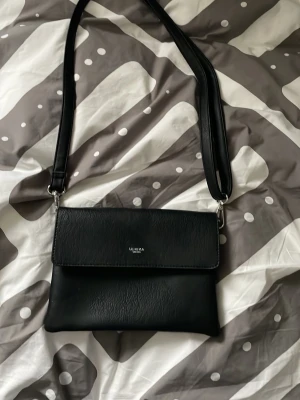 Svart axelväska från Ulrika Sweden - Snygg svart axelväska från Ulrika Sweden i stilren design. Väskan har ett slätt konstlädermaterial, magnetlås och justerbar axelrem. Perfekt storlek för det viktigaste och enkel att matcha till olika outfits. Den enda gången den här har använts var på min bal. 