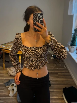 Leopardmönstrad croppad blus - Säljer en snygg leopardmönstrad blus med lång ärm och croppad passform. Toppen har volangdetaljer vid midjan och är tillverkad i ett mjukt syntetmaterial. 