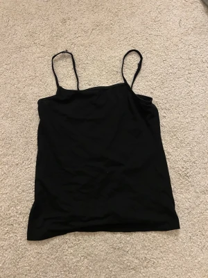Svart linnetopp från H&M - Enkel svart linnetopp från H&M med tunna axelband och rak passform. Perfekt att också använda som en mini kjol om man skulle vela det. 