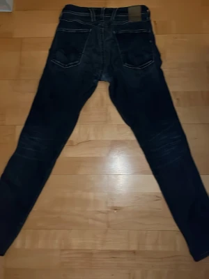 Replay Anbass Hyperflex jeans, svart - Säljer ett par Replay Anbass Hyperflex jeans i svart med snygga slitningar och kontrastsömmar. Slim fit-modell med klassiska fem fickor och stretchigt material som sitter riktigt skönt. Perfekta om du gillar en modern och clean look.