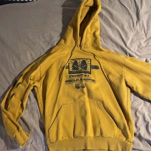 Gul Carhartt hoodie med tryck, S - Gul hoodie från Carhartt Work In Progress i storlek S, stor i storleken. Framsidan har ett grafiskt tryck. Tröjan har huva med snörning och stor magficka. Perfekt statement-plagg för dig som gillar streetwear. 