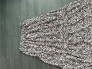 Blommig långkjol från Kappahl - Supersöt långkjol från Kappahl med småblommigt mönster i svart, lila, rosa och grönt. Kjolen har resår i midjan och är luftig med flera volanger. Perfekt för dig som gillar en romantisk och chill stil.