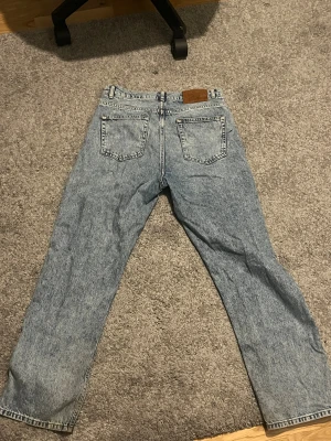 Blå straight jeans från Grunt - Säljer ett par blå tvättade jeans från Grunt med klassisk femficksdesign och raka ben. Jeansen har en ljusblå, stentvättad look och kontrastsömmar i gult. Materialet är robust denim och passformen är straight. Perfekt för dig som gillar retrovibbar och enkel stil.