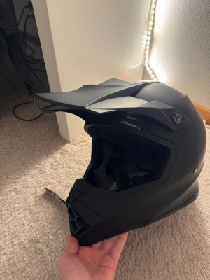 Svart motocrosshjälm endast öppnad - Säljer en svart motocrosshjälm med cool, kantig design. Insidan har mjuk, ventilerande mesh och justerbart hakband. Perfekt för dig som gillar fart och äventyr på två hjul. Snygg och funktionell look som sticker ut.