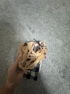 Beige rutig halsduk med fransar - Snygg beige halsduk från Burberry med klassiskt rutigt mönster i svart, vitt och rött. Mjukt material och fransar i kanterna som ger en chill vibe. Perfekt att slänga över axlarna när det är kallt ute. Ikonisk design som aldrig går ur tiden.