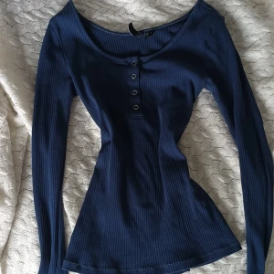 Elena Gilbert tröja - Säljer en mörkblå ribbad långärmad topp från Nelly Toppen har rund halsringning och fyra dekorativa metallknappar framtill. Snygg och figurnära passform, perfekt till jeans eller kjol.