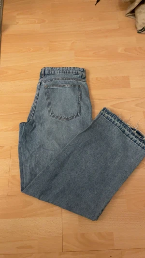 Blå wide jeans från H&M Divided - Säljer ett par ljusblå jeans från H&M Divided i storlek 38. Modellen är wide med raka ben och rå, fransig kant nedtill för en cool och avslappnad vibe. Klassisk femficksdesign och midwaist. Perfekta att styla med sneakers eller boots.