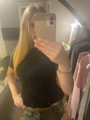 Marinblå topp från Gina med volangkant - Säljer en marinblå  topp med korta ärmar och volangkant nedtill. Toppen har en ribbad struktur som ger en cool och modern känsla. Passformen är normal och toppen är croppad, vilket gör den perfekt till jeans eller kjol. Materialet känns mjukt och stretchigt.