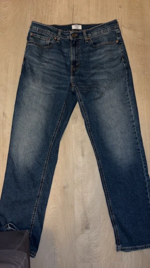 Levi's Denizen raka jeans blå 36W - Klassiska blå jeans från Levi's Denizen med raka ben och femficksmodell. Jeansen har normal passform, snygga kontrastsömmar och läderpatch bak i midjan. Tillverkade i slitstarkt denimtyg som ger en tidlös look.