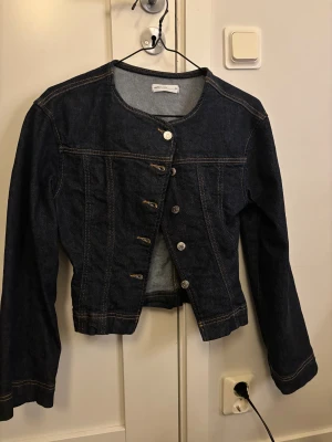 Mörkblå jeansjacka från Perfect Jeans - Snygg mörkblå jeansjacka från Perfect Jeans i storlek XS. Klassisk modell med rund hals, kontrastsömmar och silverfärgade knappar framtill. Jackan har lång ärm och är perfekt för dig som gillar en clean och tidlös look.