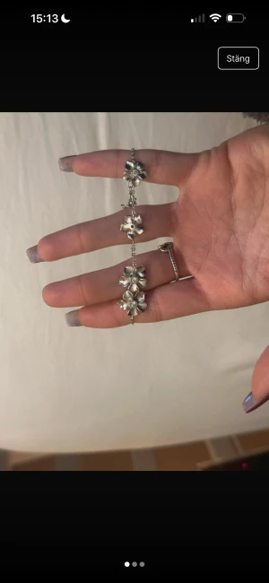 Silverfärgat armband med blommor - Snyggt armband i silverfärg med flera blommor som hänger längs en tunn kedja. Blommorna har en detaljerad design och ger ett coolt och unikt intryck. Perfekt för dig som gillar smycken med lite extra karaktär och blommiga detaljer.