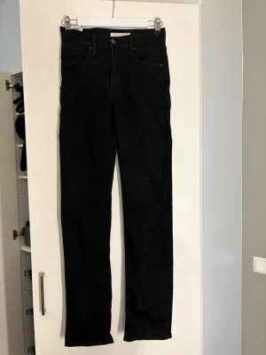 Levi's 724 High Rise Straight svarta jeans - Svarta Levi's 724 High Rise Straight jeans med klassisk femficksdesign och raka ben. Hög midja för en snygg siluett och stilren look. Tillverkade i mjukt denimtyg som sitter bekvämt hela dagen.