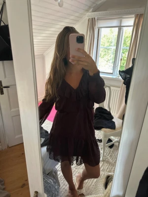 Vinröd volangklänning med prickar - Supersöt vinröd kortklänning med små prickar och volangdetaljer vid halsringningen och nederkanten. Klänningen har långärmade transparenta ärmar och markerad midja. Perfekt för dig som gillar romantisk stil!